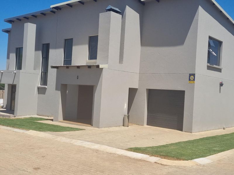 Front elevation of a modern townhouse featuring a paved driveway, integrated garage, and covered entrance area with neutral exterior finishes.