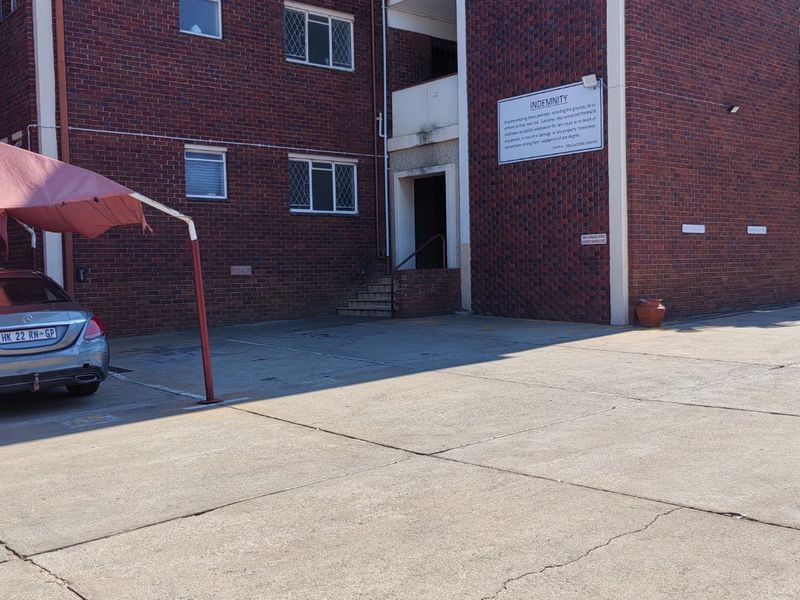 Exterior view of a brick apartment building featuring a concrete driveway, carport structure, and building entrance.