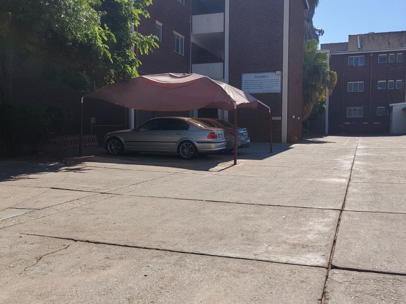Exterior view of an apartment complex featuring a brick facade and a paved parking area with a carport structure.