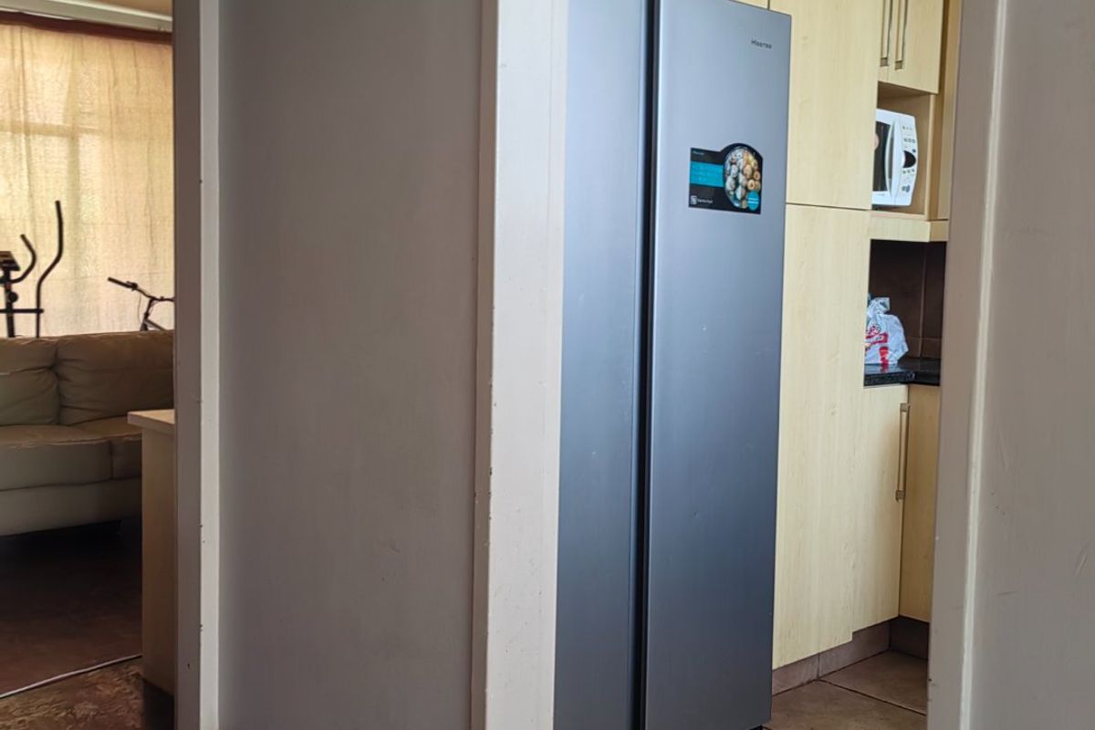 A view into a kitchen featuring light wood cabinetry and tiled flooring, adjacent to a living area with parquet flooring.