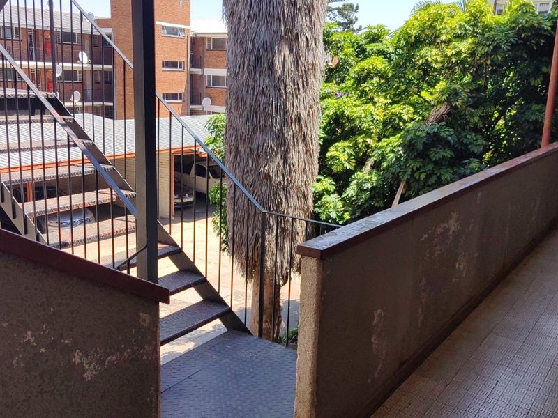 An outdoor balcony area featuring a metal staircase, tiled flooring, and concrete balustrades, overlooking the apartment complex grounds.
