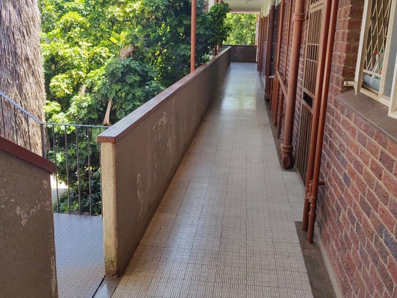 An exterior apartment walkway featuring tiled flooring, brick walls, and security gates, providing access to units.