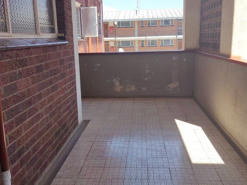 A covered balcony featuring tiled flooring, brick wall accents, and a breeze block screen, offering an outdoor space with potential for improvement.