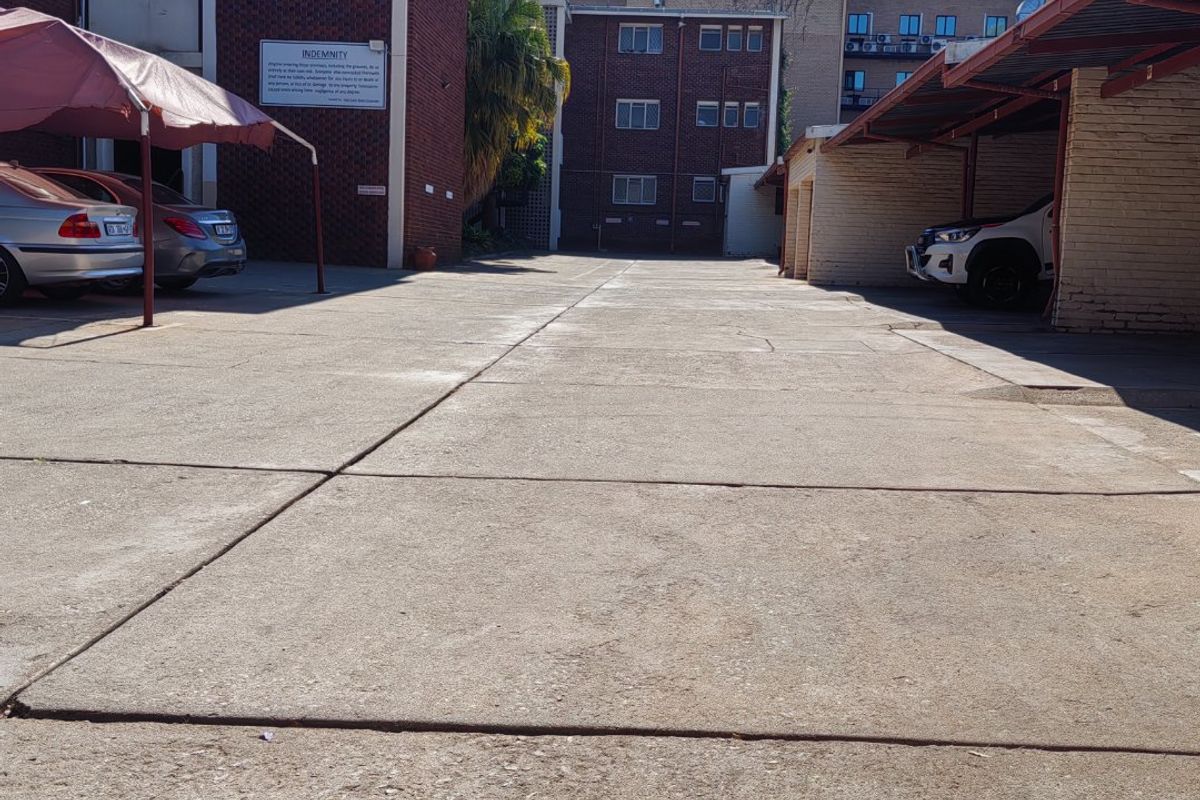 Exterior view of an apartment complex parking area featuring a concrete driveway, covered carports, and brick building facades.