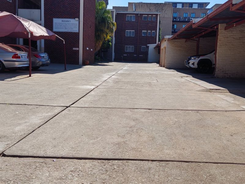 Exterior view of an apartment complex parking area featuring a concrete driveway, covered carports, and brick building facades.