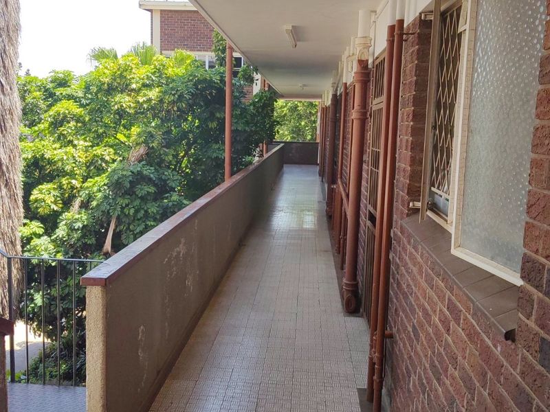 An exterior apartment walkway featuring tiled flooring, brick wall construction, and security window bars, providing access to residential units.