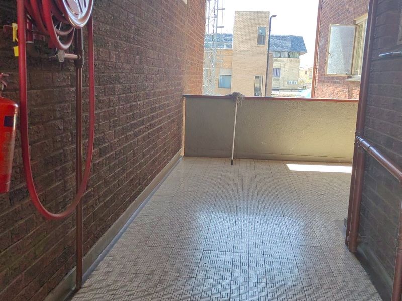A functional outdoor balcony area featuring brick walls, tiled flooring, and essential fire safety equipment, providing a practical transition space.