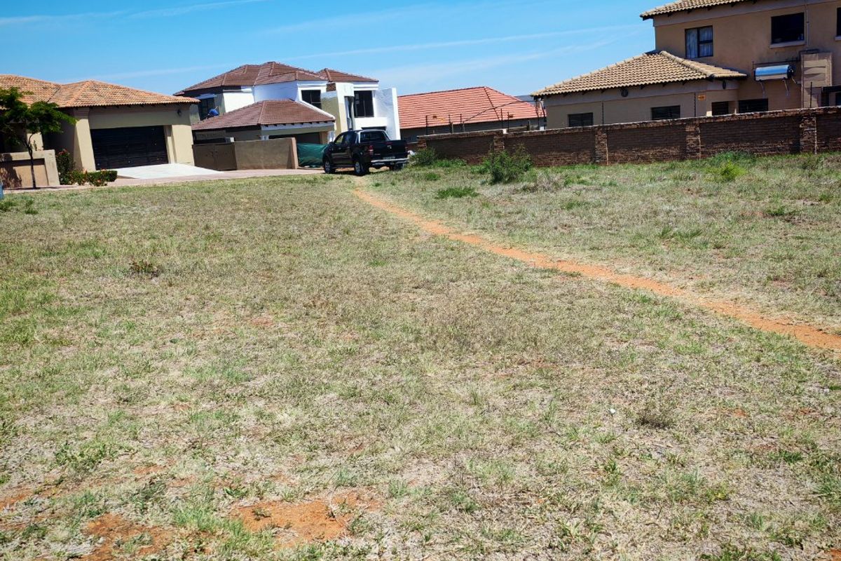A vacant residential plot of land situated in a developed neighborhood, featuring grassed terrain and perimeter boundary walls.