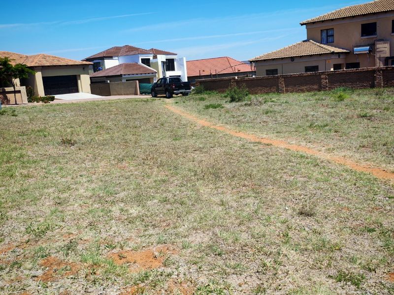 A vacant residential plot of land situated in a developed neighborhood, featuring grassed terrain and perimeter boundary walls.