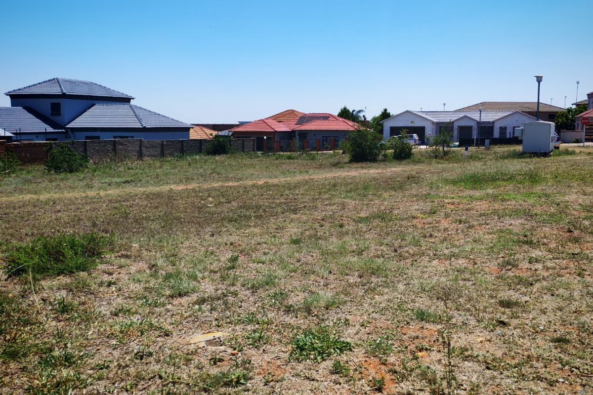 A vacant residential plot of land situated in a developed neighborhood, featuring natural ground cover and boundary walling.