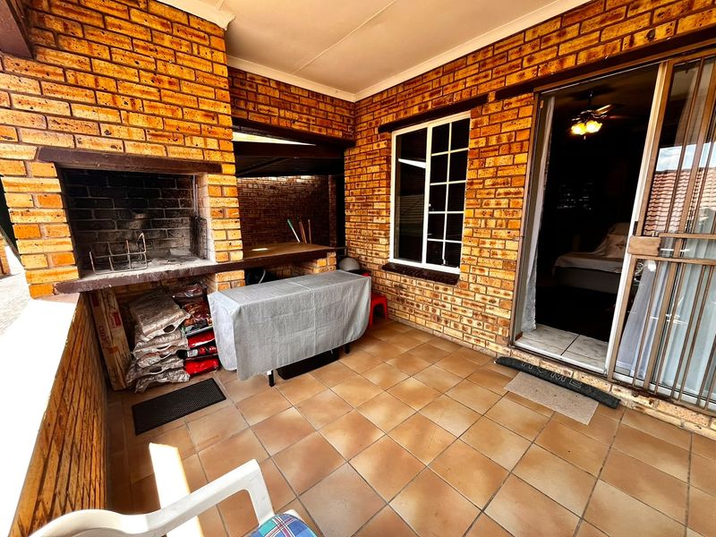 Covered patio area featuring a built-in brick braai, tiled flooring, and direct access to the interior through a sliding glass door.