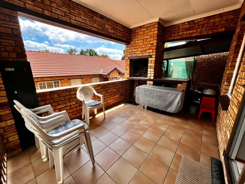 Covered patio featuring exposed brick walls, tiled flooring, and a built-in brick braai, offering a functional outdoor entertainment space.