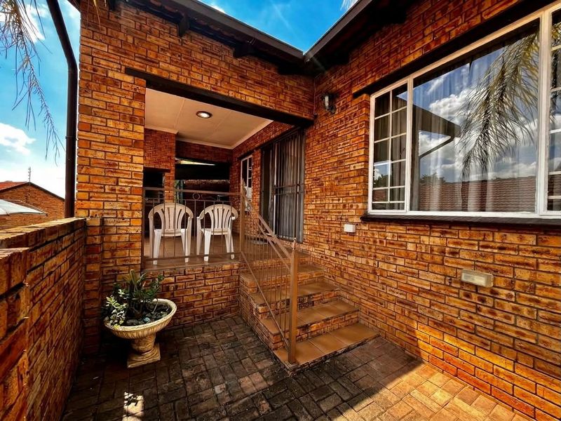 A charming brick-clad patio area featuring a paved courtyard, tiled steps with metal railings, and a covered outdoor space with recessed lighting.