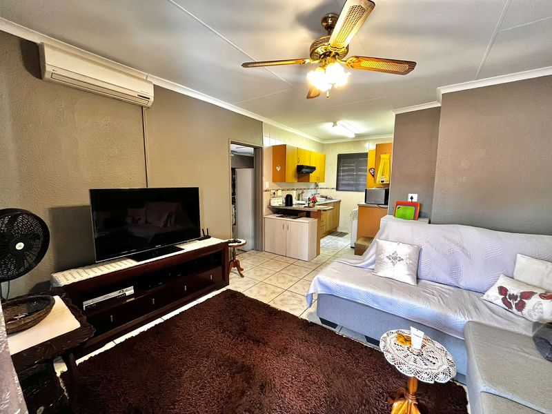 Open-plan living area featuring tiled floors, a ceiling fan, and a split-system air conditioner, flowing into a functional kitchen space.