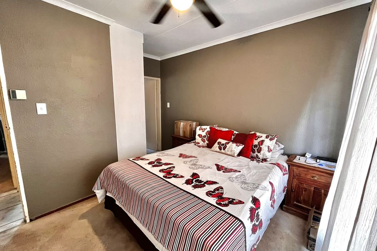 A standard bedroom featuring a ceiling fan, carpeted flooring, and neutral wall finishes, offering a functional space ready for cosmetic updates.