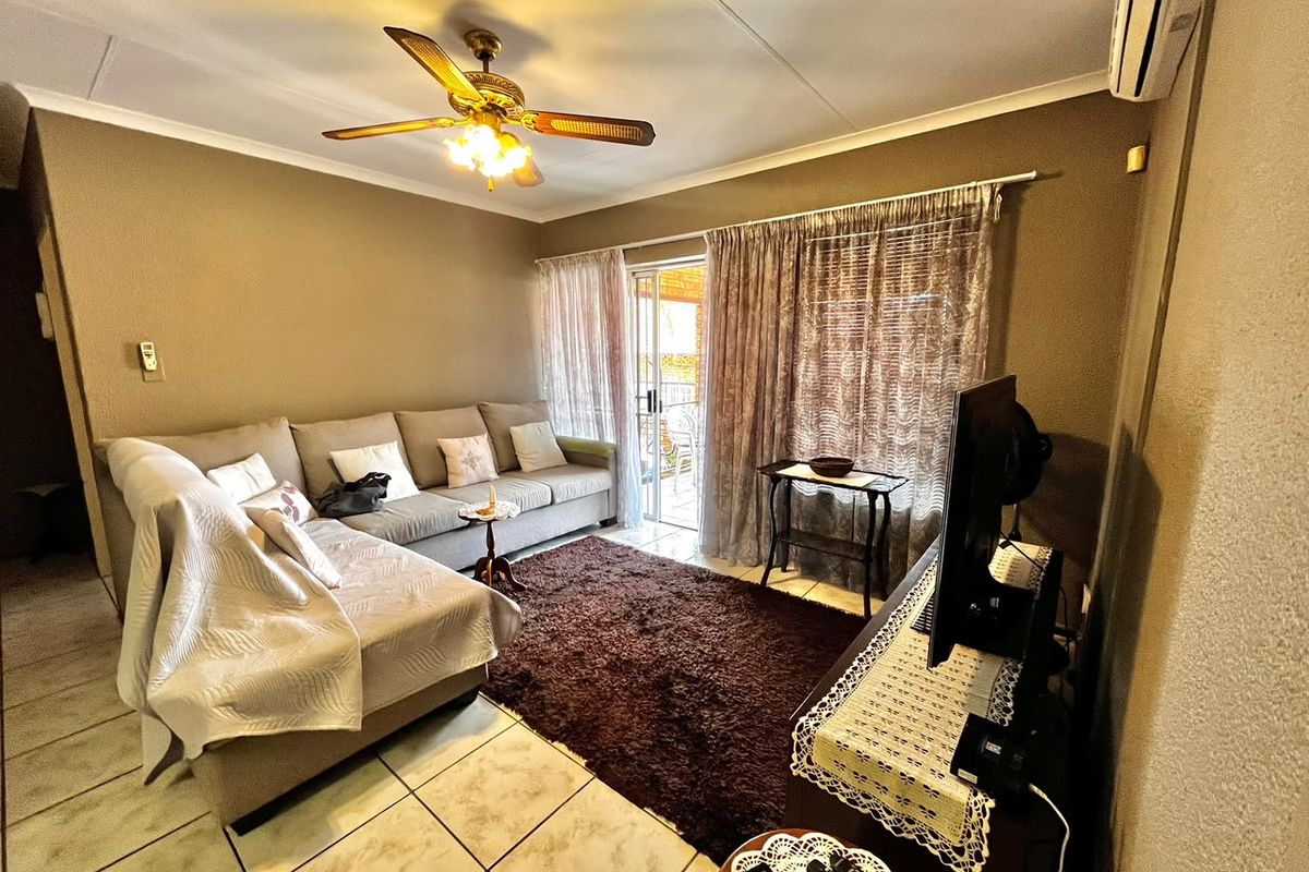 A comfortable living room featuring tiled flooring, a ceiling fan, and a split-system air conditioner, with direct access to an outdoor patio area.