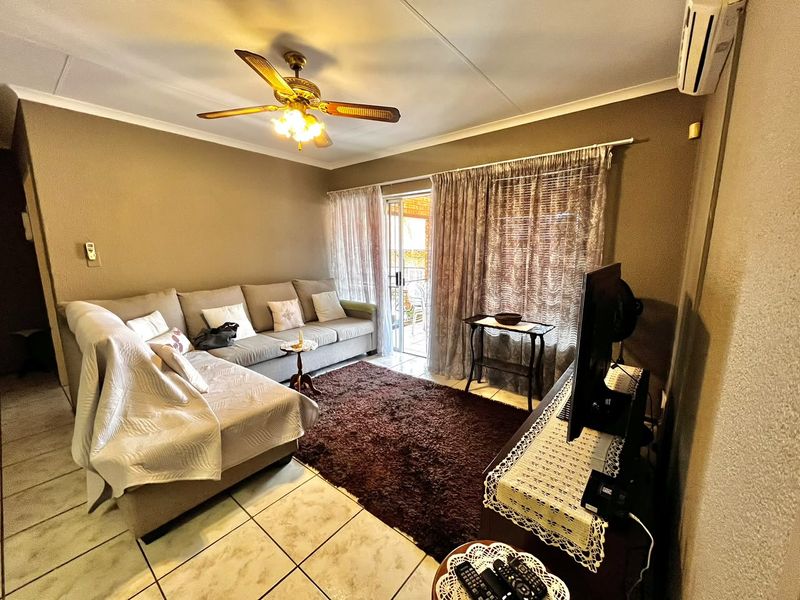 A comfortable living room featuring tiled flooring, a ceiling fan, and a split-system air conditioner, with direct access to an outdoor patio area.