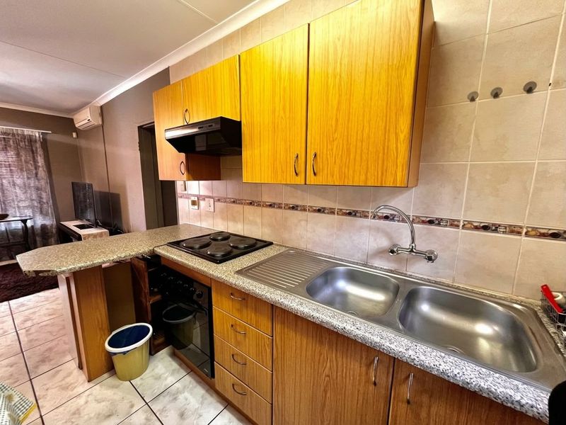 Compact kitchen featuring wood-look cabinetry, granite-style laminate countertops, a double stainless steel sink, built-in oven, and electric hob with an integrated breakfast bar.