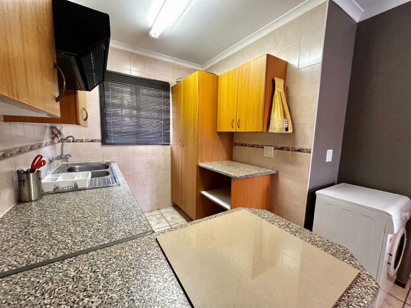 Functional kitchen featuring laminate cabinetry, granite countertops, double bowl sink, and tiled splashbacks, providing a practical workspace with integrated storage.