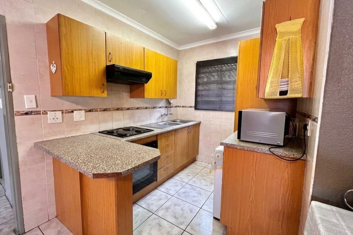 Functional kitchen featuring wood-finish cabinetry, laminate countertops, built-in oven, electric hob, and tiled flooring, offering a practical layout for daily meal preparation.