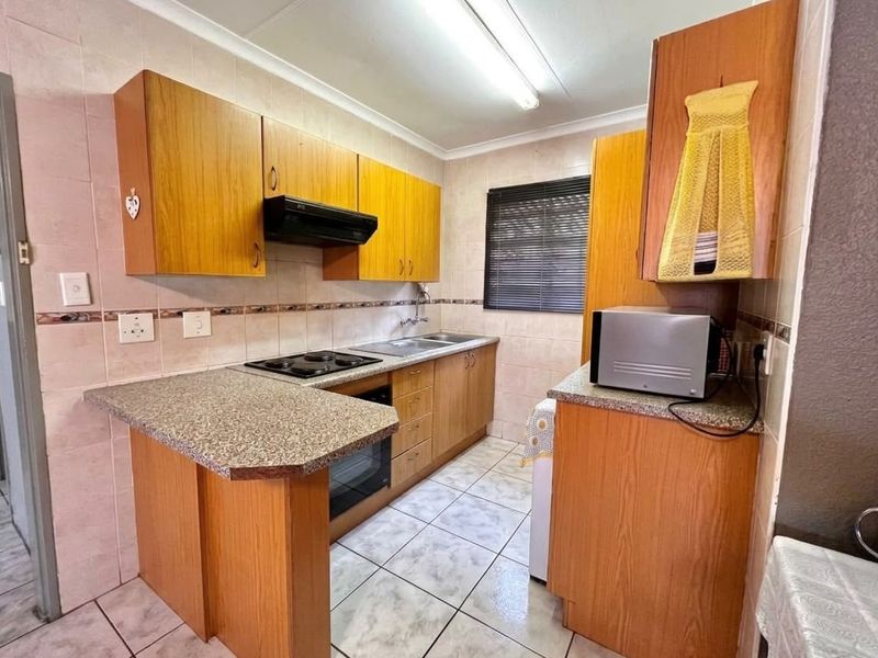 Functional kitchen featuring wood-finish cabinetry, laminate countertops, built-in oven, electric hob, and tiled flooring, offering a practical layout for daily meal preparation.