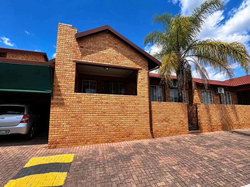 Front elevation of a face brick townhouse featuring a covered patio, paved driveway, and secure entrance.