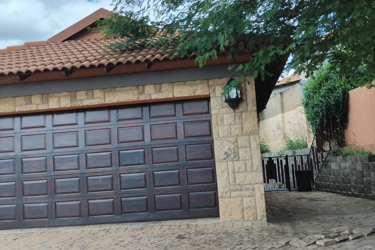 Front elevation of the property featuring a double garage with stone cladding, tiled roof, and paved driveway access.