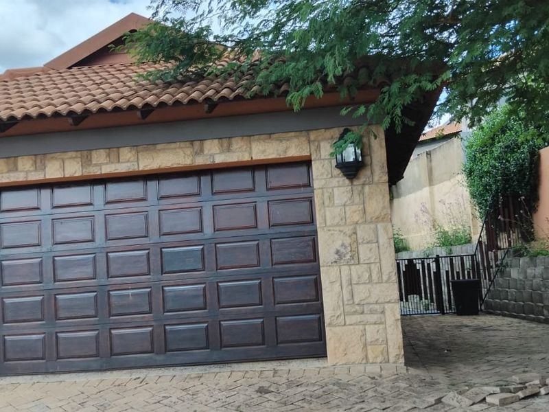 Front elevation of the property featuring a double garage with stone cladding, tiled roof, and paved driveway access.