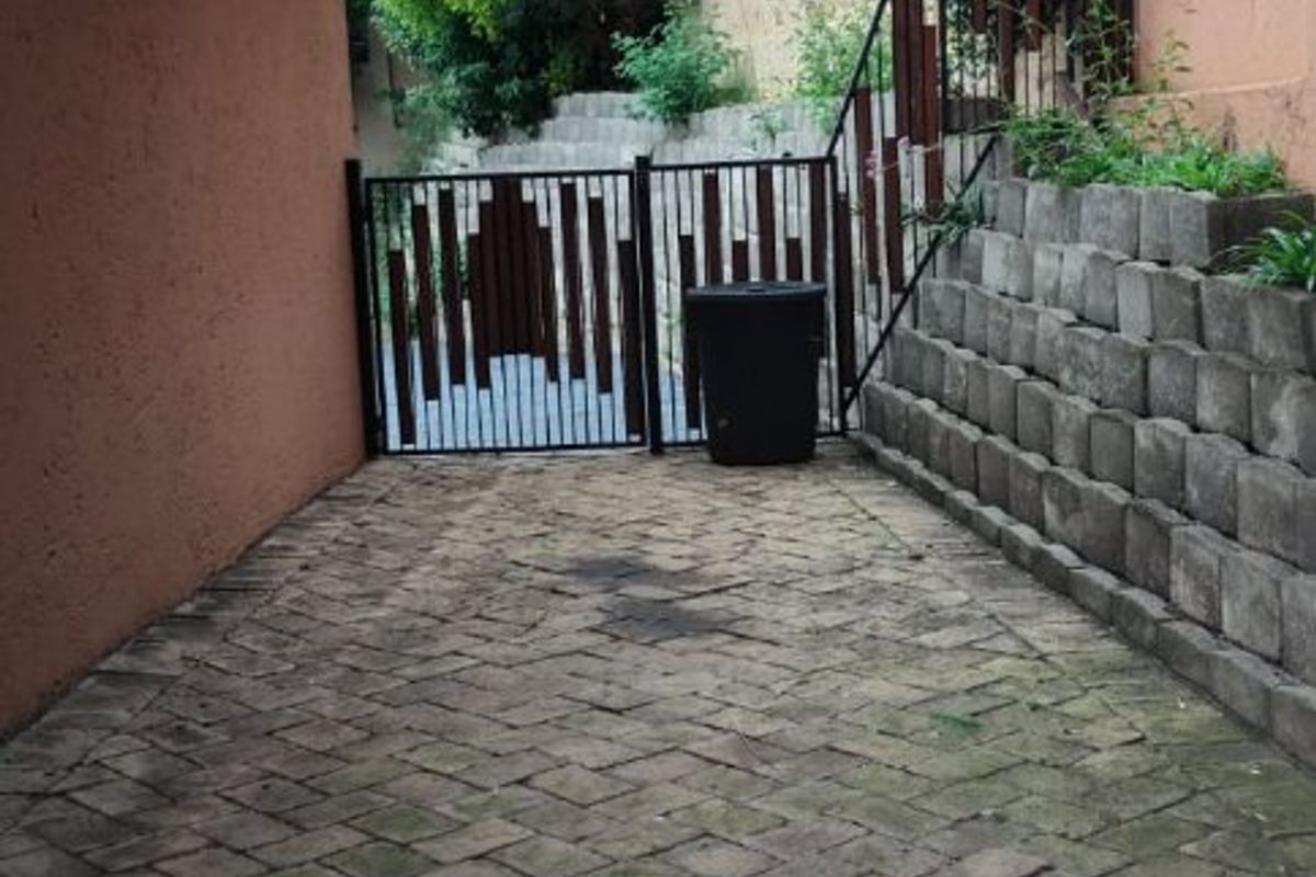 A paved side walkway featuring a retaining wall, metal security gate, and exterior wall lighting.
