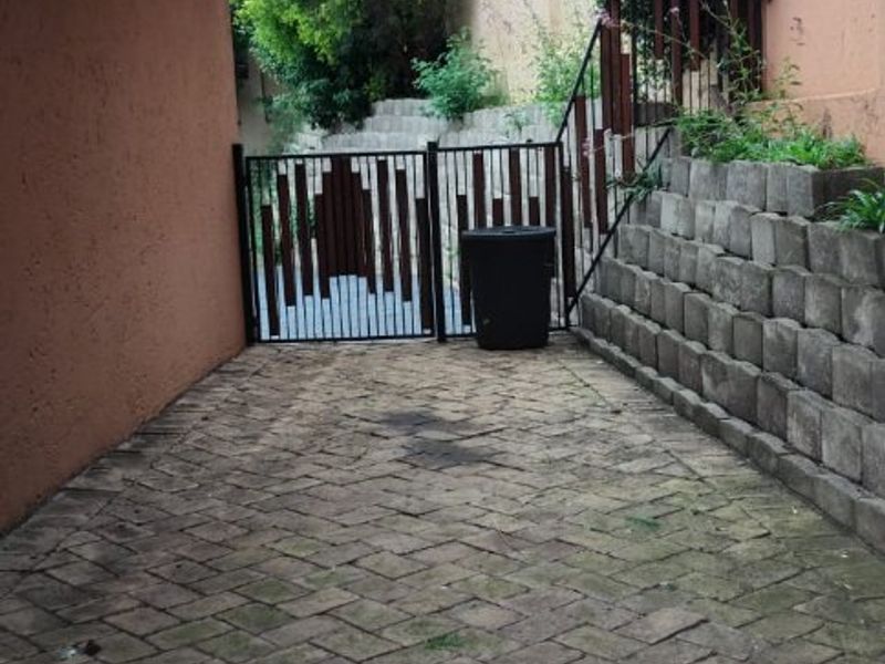 A paved side walkway featuring a retaining wall, metal security gate, and exterior wall lighting.
