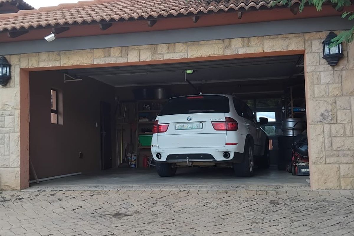 A double garage featuring stone cladding, a tiled roof, and exterior wall lighting, accessible via a paved driveway.