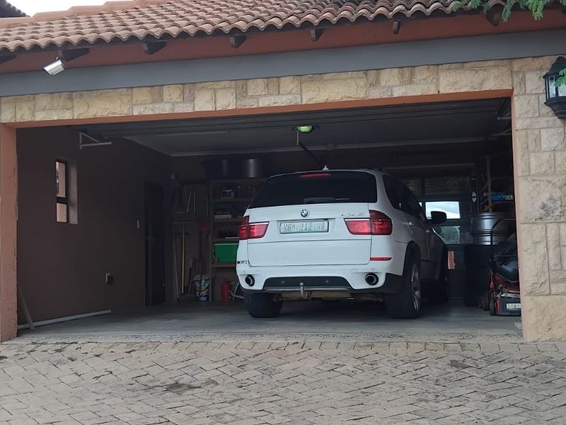 A double garage featuring stone cladding, a tiled roof, and exterior wall lighting, accessible via a paved driveway.