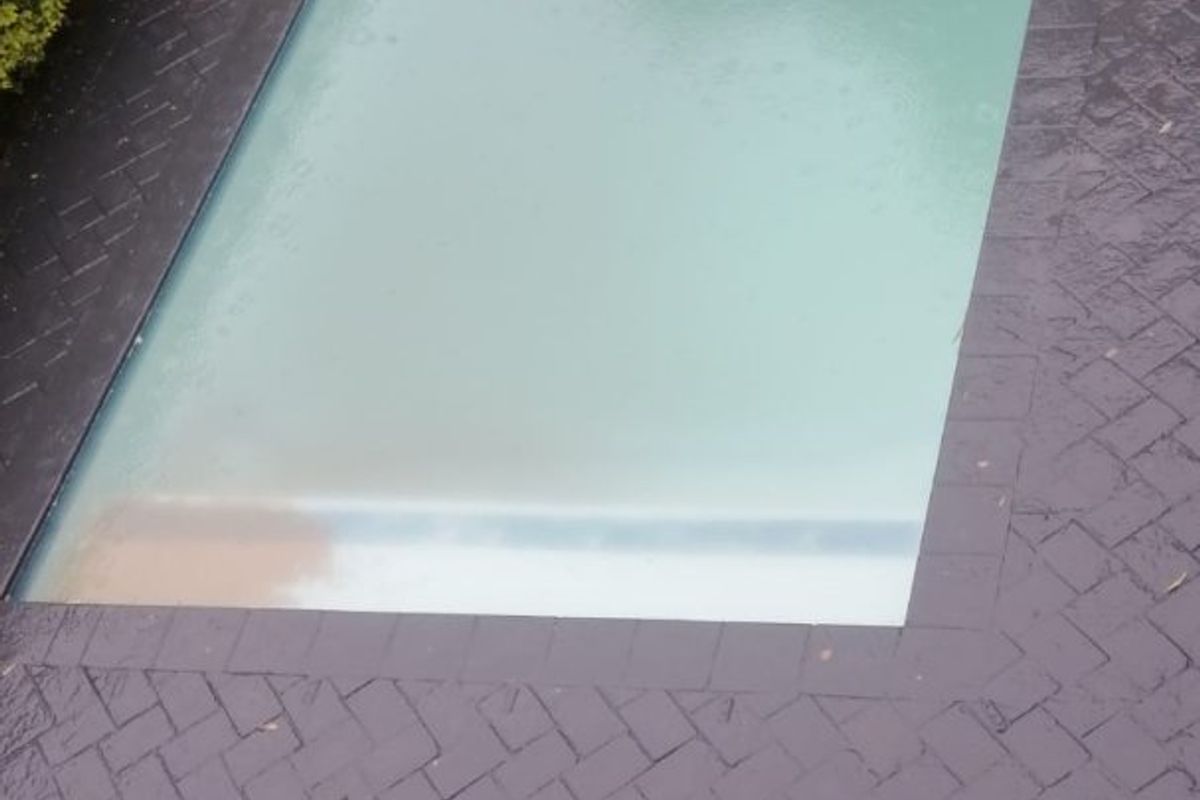 An outdoor swimming pool area featuring dark herringbone brick paving and a boundary wall.