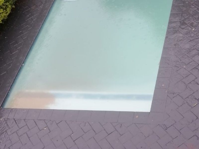 An outdoor swimming pool area featuring dark herringbone brick paving and a boundary wall.