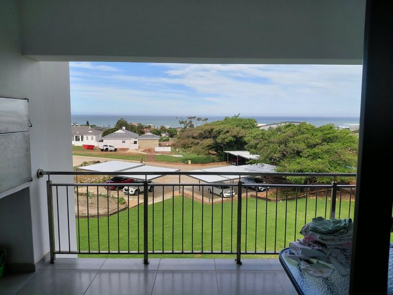 A covered balcony featuring a stainless steel balustrade and tiled flooring, offering an elevated view of the surrounding grounds and distant ocean.