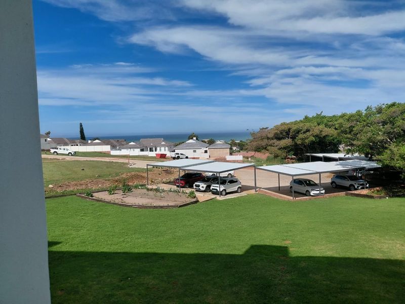 An elevated view overlooking a communal garden area with covered parking bays and a distant coastal horizon.