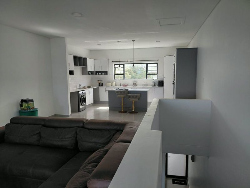 Modern open-plan living area featuring a contemporary kitchen with a central island, sleek cabinetry, and subway tile backsplash, overlooking the staircase.