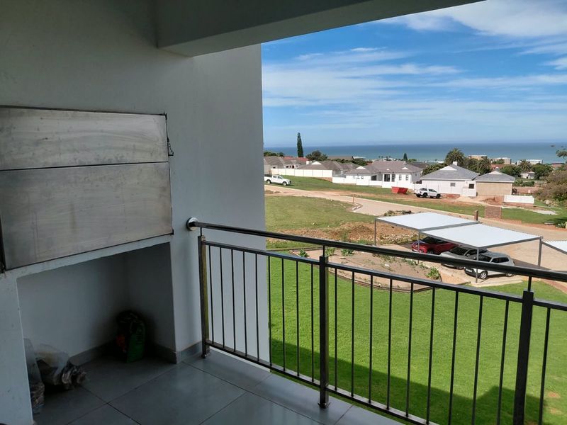 Covered balcony featuring a built-in braai, stainless steel balustrade, and tiled flooring, offering scenic views of the surrounding neighborhood and coastline.