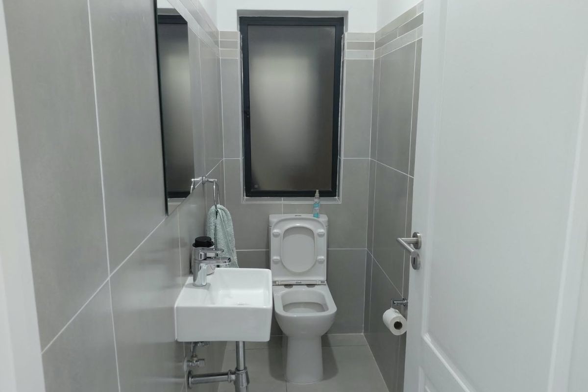 A compact, modern bathroom featuring grey ceramic wall and floor tiles, a wall-mounted basin with chrome fixtures, and a toilet.