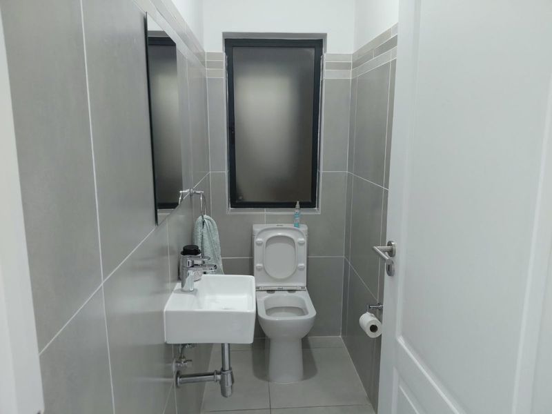 A compact, modern bathroom featuring grey ceramic wall and floor tiles, a wall-mounted basin with chrome fixtures, and a toilet.
