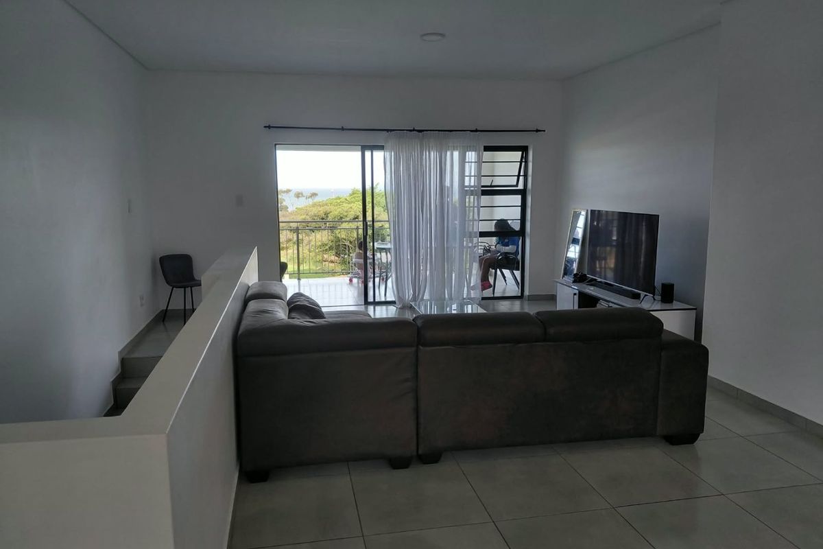 Spacious living area featuring neutral tiled flooring, recessed lighting, and direct access to a private balcony through large sliding glass doors.