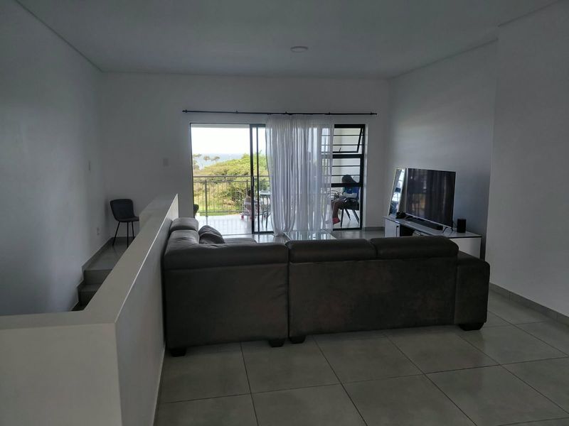 Spacious living area featuring neutral tiled flooring, recessed lighting, and direct access to a private balcony through large sliding glass doors.