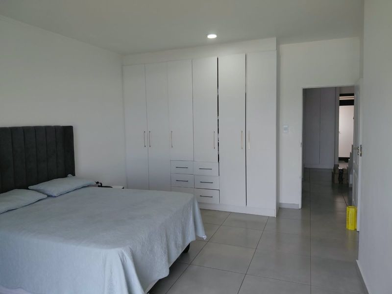 A spacious bedroom featuring neutral tiled flooring, ample built-in cupboard storage, and modern recessed downlighting.