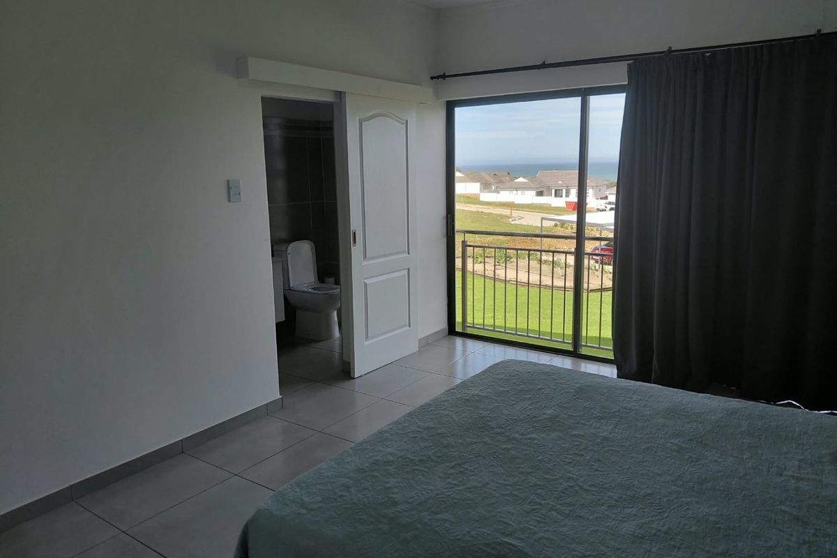 A bedroom featuring tiled flooring, a sliding door leading to a balcony with coastal views, and direct access to an en-suite bathroom.