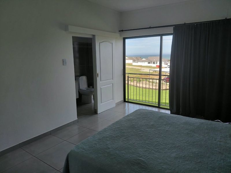 A bedroom featuring tiled flooring, a sliding door leading to a balcony with coastal views, and direct access to an en-suite bathroom.