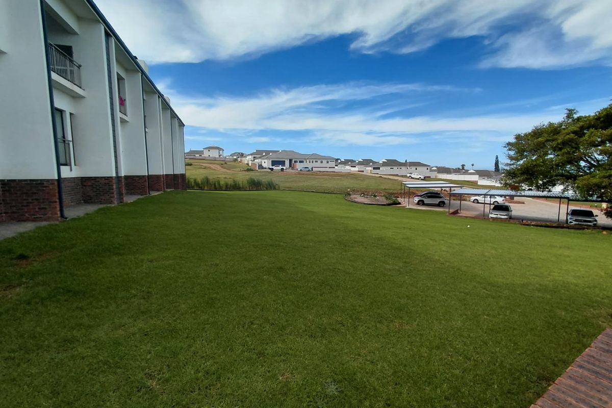 A view of the rear exterior of the apartment building featuring a large lawn area and a covered carport structure.