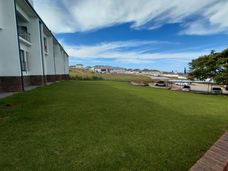 A view of the rear exterior of the apartment building featuring a large lawn area and a covered carport structure.
