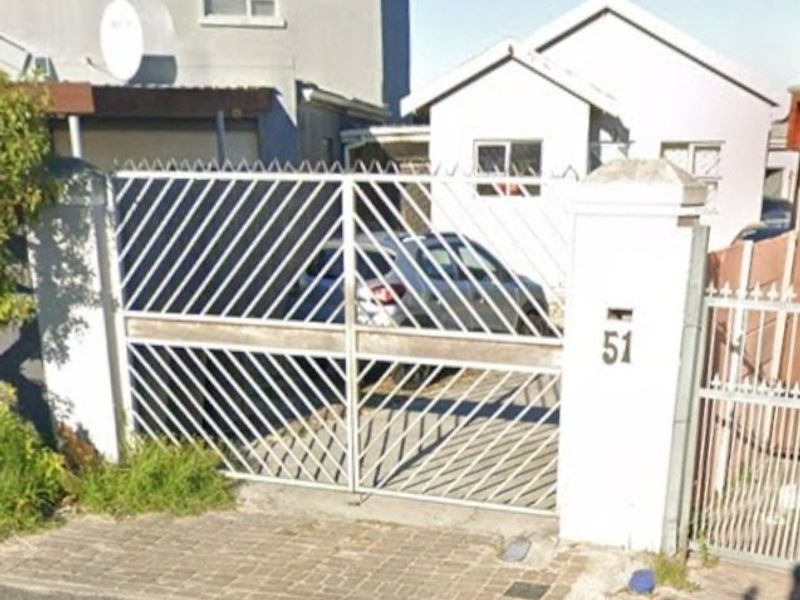 Front elevation of the property featuring a secure metal gate, masonry pillars, and a paved driveway entrance.