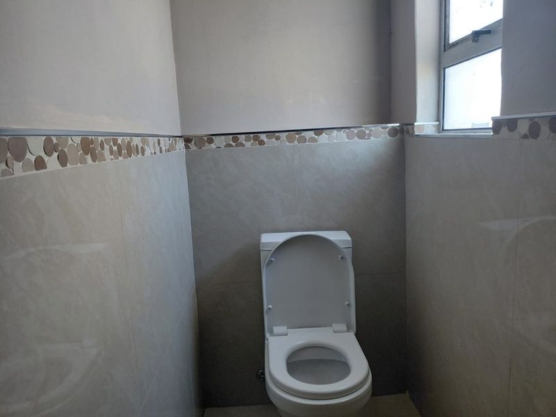 A compact bathroom featuring neutral wall tiles with a decorative border and a standard toilet.
