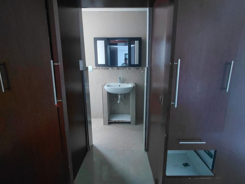 A small bathroom area featuring a pedestal washbasin, wall-mounted mirror cabinet, and built-in storage cupboards with some visible wear and missing hardware.